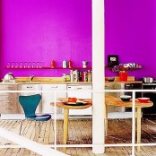 a vibrant kitchen with a hot pink wall, neutral cabinetry, wooden tables and a navy chair is a fantastic statement