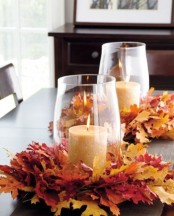 oversized glasses with pillar candles placed on large faux leaf wreaths form amazing bold centerpieces for a fall tablescape