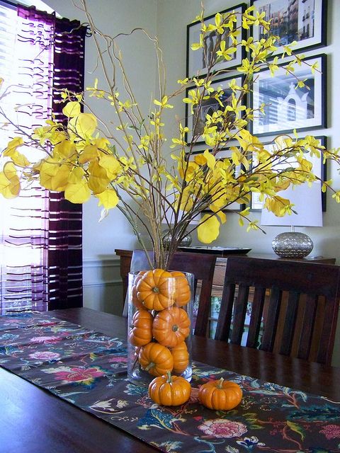 a bright and simple fall centerpiece of a clear vase filled with mini pumpkins and branches with yellow leaves