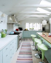 a pastel kitchen with powder cabinets, green stools, stainless steel appliances and striped rugs is cheerful and cool