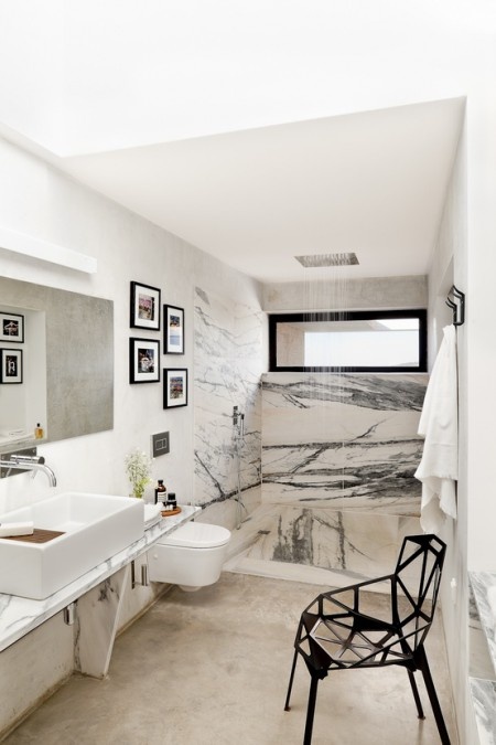 a neutral bathroom done with a concrete floor, white and black marble in the shower space and a black geometric chair
