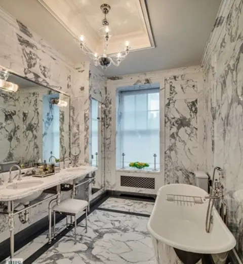 A luxurious vintage inspired bathroom clad with white marble completely, with a metallic tub and sinks on stands