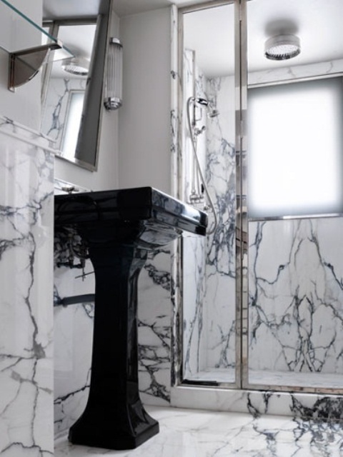 A tiny yet luxurious bathroom done with white and black marble, with a shower space and a black free standing sink