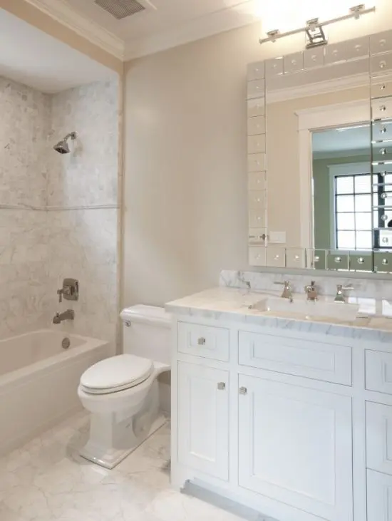 a chic neutral bathroom with marble tiles on the floor and in the tub space, a marble clad vanity and a stylish mirror
