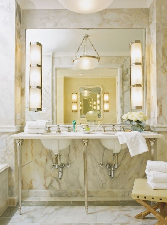 an elegant and chic warm-colored marble bathroom with many lamps, a sink on a stand and a large mirror
