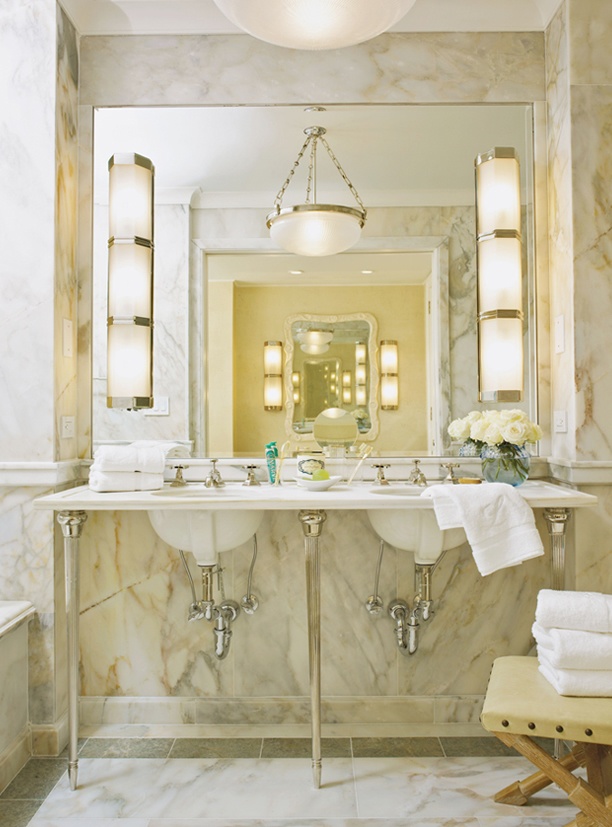 An elegant and chic warm colored marble bathroom with many lamps, a sink on a stand and a large mirror