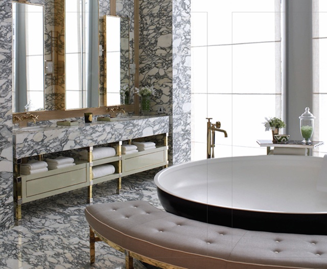 A unique bathroom with a round tub, a pink curved bench, a built in vanity and much black and white marble