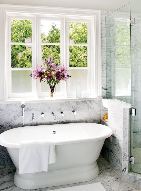a chic and refined white marble bathroom with an oval vintage tub and a large window to enjoy the views