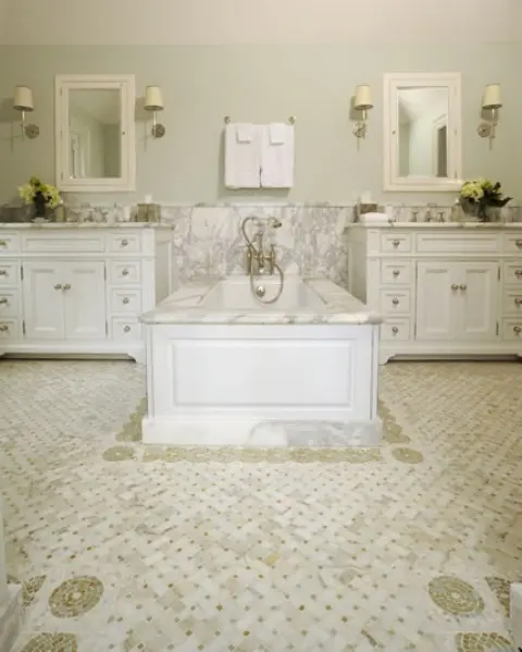 A vintage inspired white bathroom with white vanities and a tile floor and a sink zone with white marble plus a tub clad with it, too
