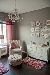 a vintage nursery with grey walls, a creamy chair and a footrest, a white dresser, a crystal chandelier and pink textiles – curtains and rugs