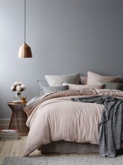 a serene grey bedroom with a bed with blush and grey bedding, a pendant lamp, a wooden stool with books