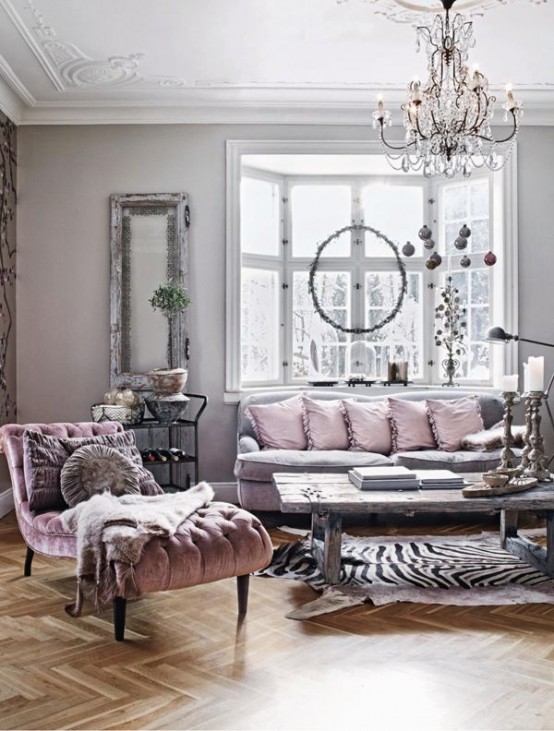 a refined and chic living room with grey walls and a bay window, a grey sofa with pink pillows, a pink lounger and a crystal chandelier
