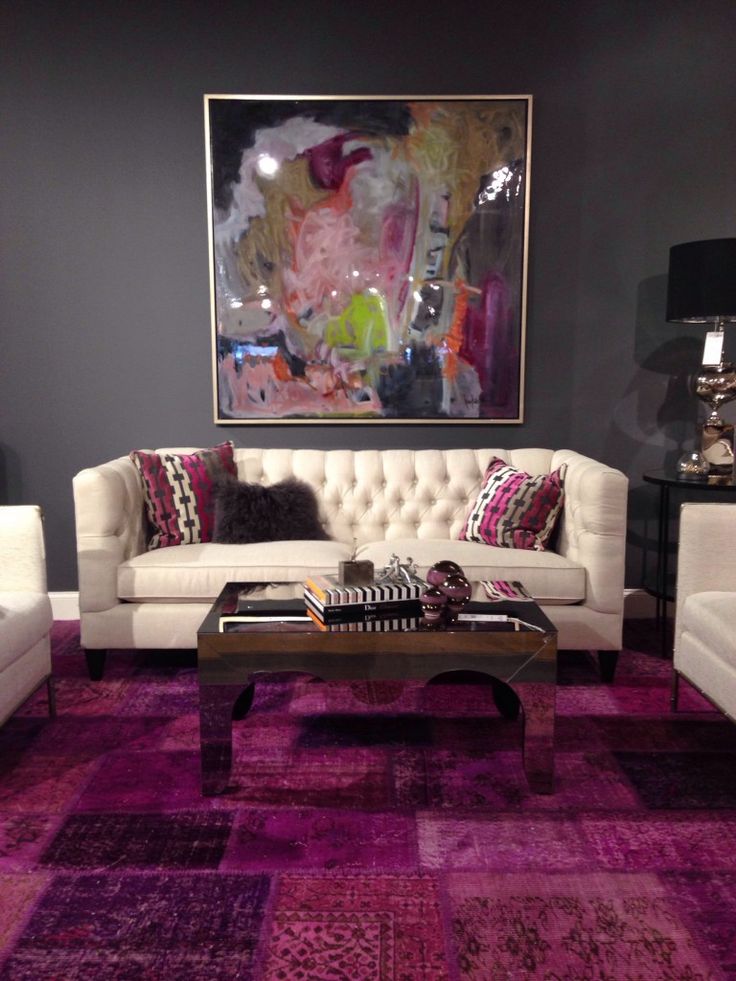 A graphite grey living room with creamy seating furniture, a glossy table, a purple rug and pink pillows, a bold artwork