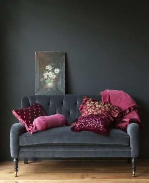a graphite grey space and a matching sofa and dark pink pillows is a stylish nook with a high contrast