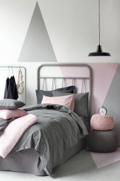 a Scandinavian kid’s room with grey and pink geometric decor on the wall, grey beds, grey and pink bedding