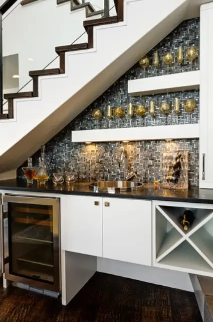 An open under the stairs home bar with a mosaic silver tile backsplash, open shelves and a fridge plus a cabinet and built in lights