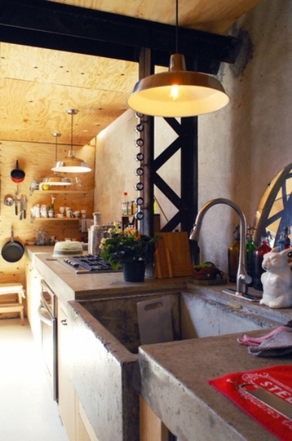 A rustic kitchen fully clad with light colored plywood and with concrete countertops and a sink for an industrial feel