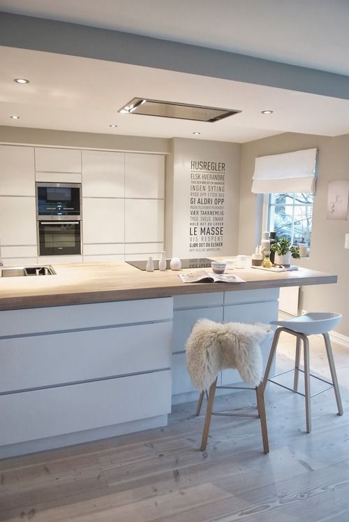 A minimalist Scandinavian kitchen with sleek white cabinets, built in lights, a large kitchen island with a small seating space and tall stools