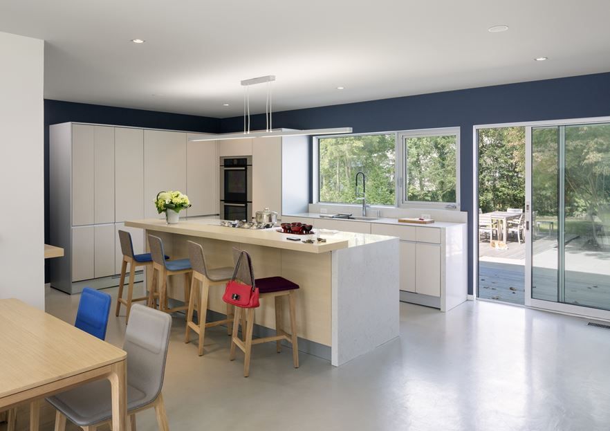 A modern white kitchen with sleek cabinets, a large kitchen island with a raised countertop for eating and having drinks here