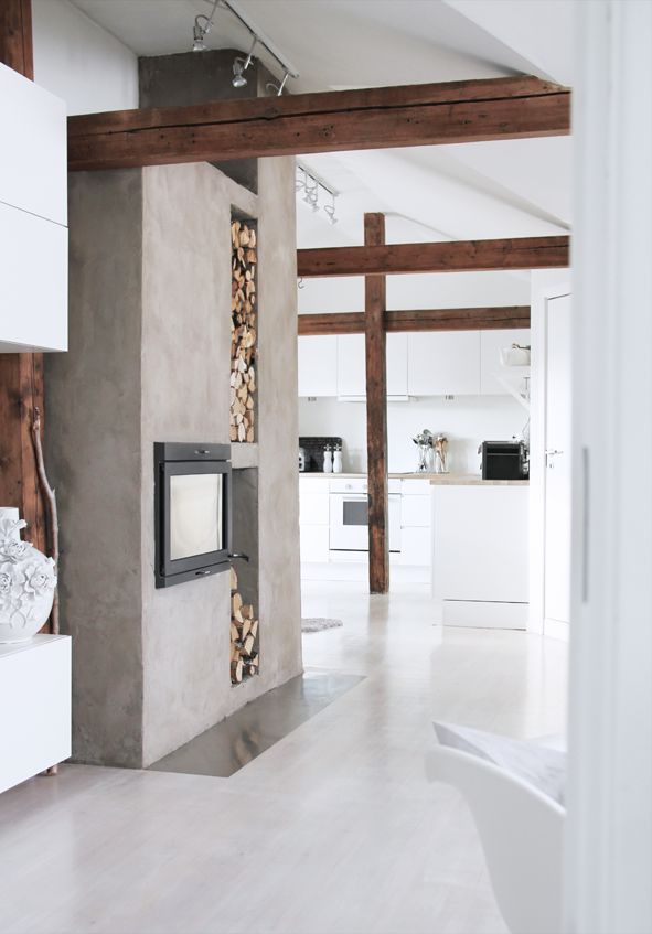 A sleek neutral space with white walls and dark stained beams, a built in fireplace, a sleek floor and a firewood storage niche