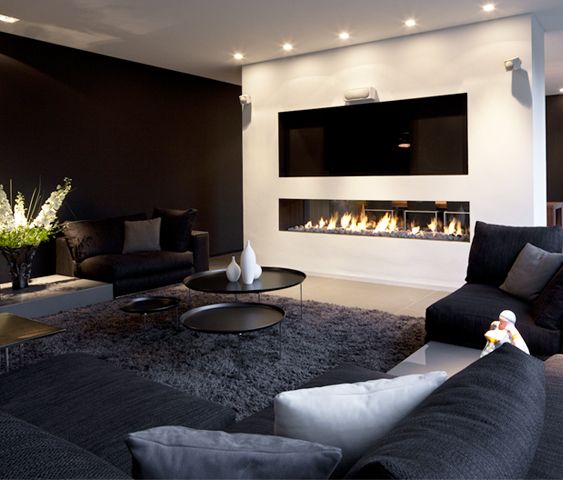 A bold black and white living room with a black accent wall, black seating furniture, a duo of black coffee tables, a built in fireplace and a TV over it