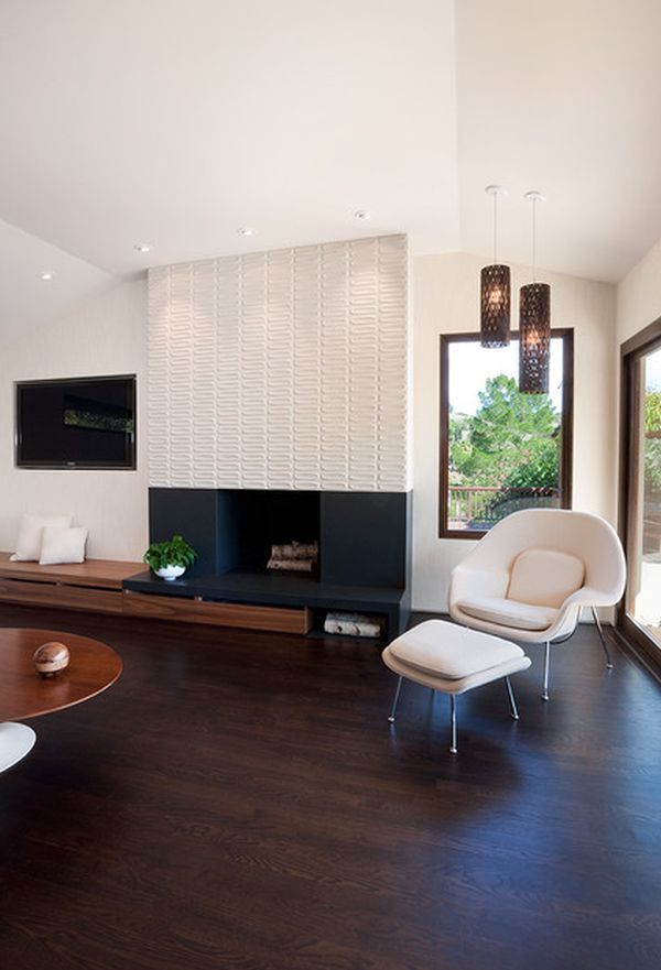 A modern living room with contrasting decor, a built in fireplace with a patterned surround, a built in bench, a creamy chair and a footrest, pendant lamps and a low coffee table and built in lights