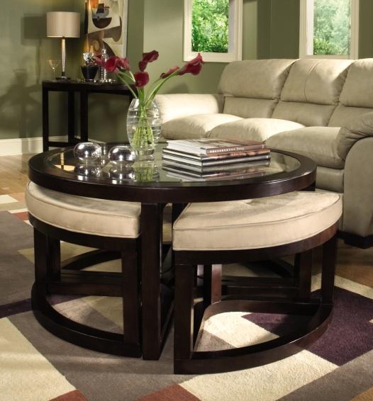 A dark staiend round coffee table with a glass tabletop and matching poufs under it to create a seating whenever needed