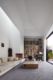 a modern double-height library with built-in shelves, a fireplace, contemporary furniture and a glass wall