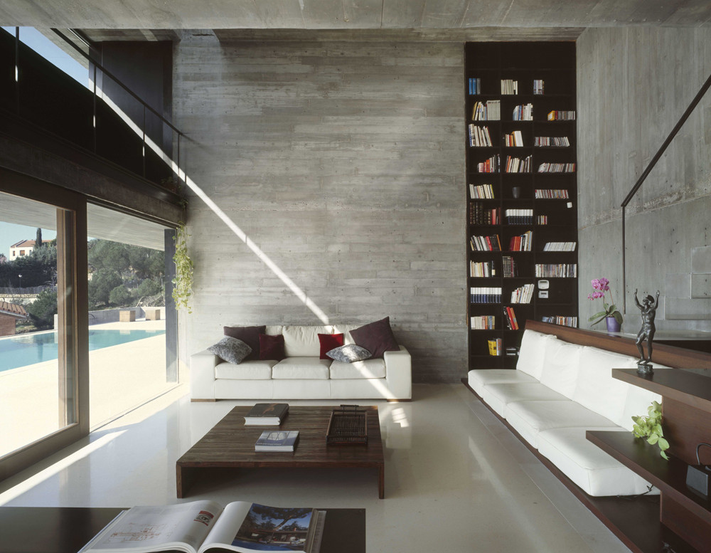 A modern to minimal home library with built in bookshelves, stylish white seatign furniture and a glazed wall for natural light