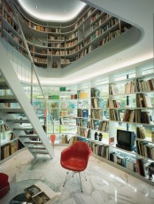 a modern sculptural library all covered with built-in bookshelves and a sculptural second floor plus a chair and much natural light