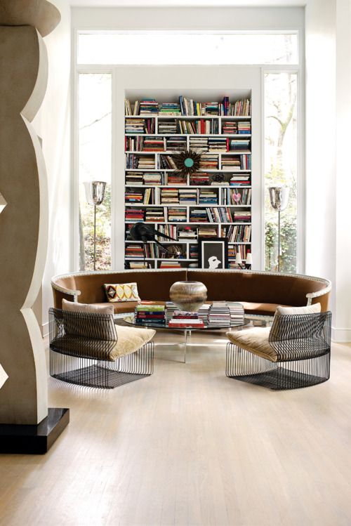 an ultra-modern library nook with bookshelves, a round leather seating, wire chairs and floor lamps