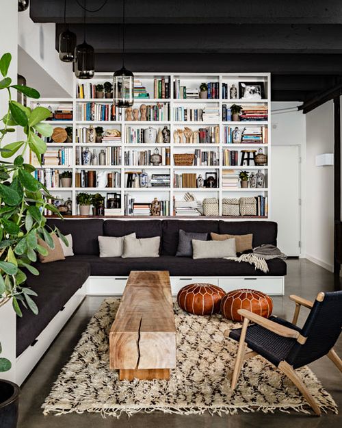 A modern black and white library with white bookshelves, an L shaped black sofa, a wooden slab table and a black chair