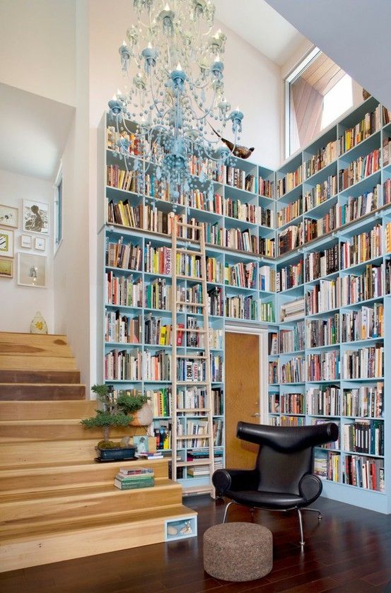 a modern library nook with very tall blue bookshelves, a blue chandelier and a black leather chair