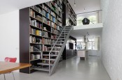 a modern home library on the go – an oversized dark bookshelf unit that is placed on the left of the steps and takes two floors