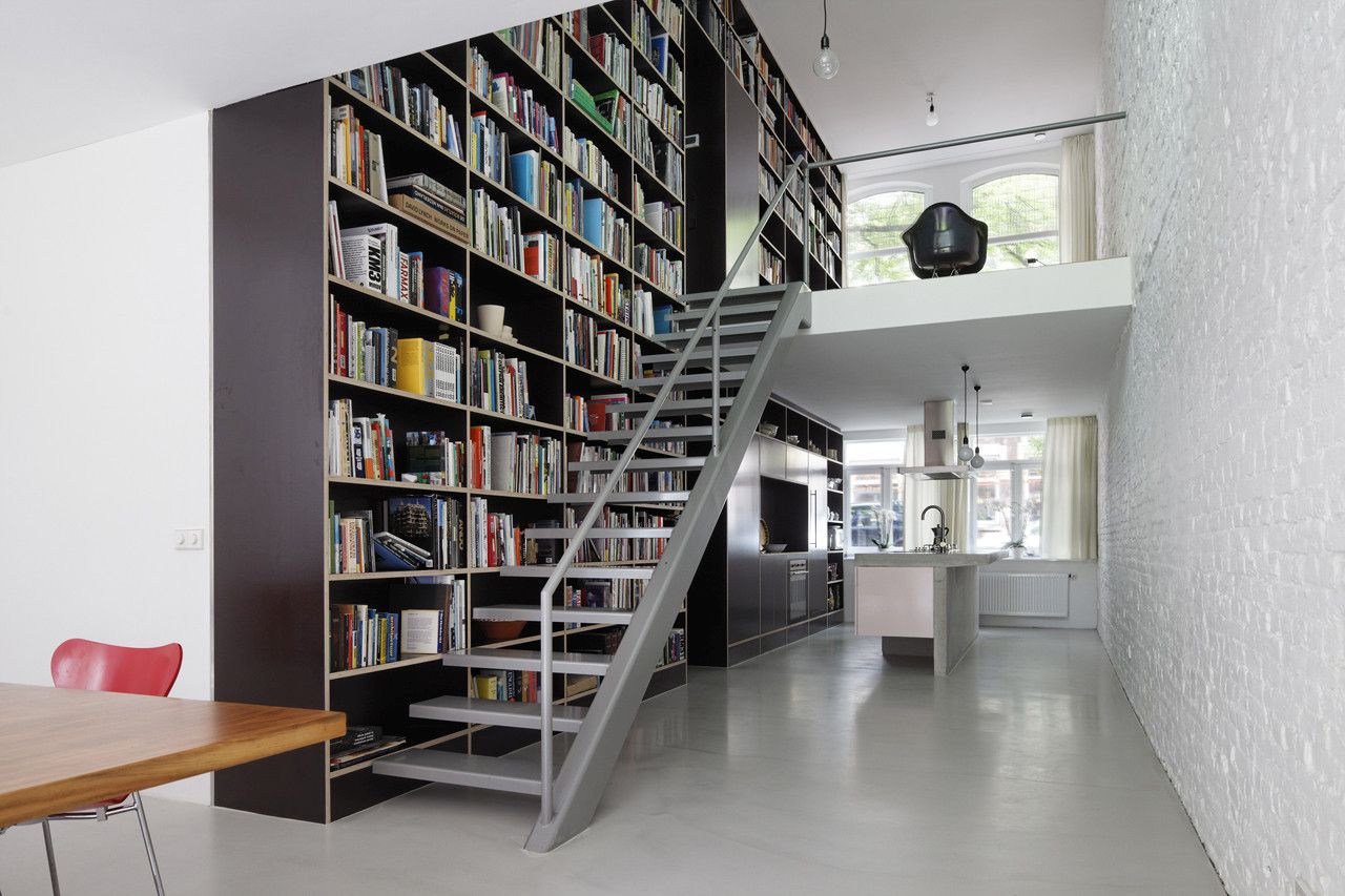 A modern home library on the go   an oversized dark bookshelf unit that is placed on the left of the steps and takes two floors