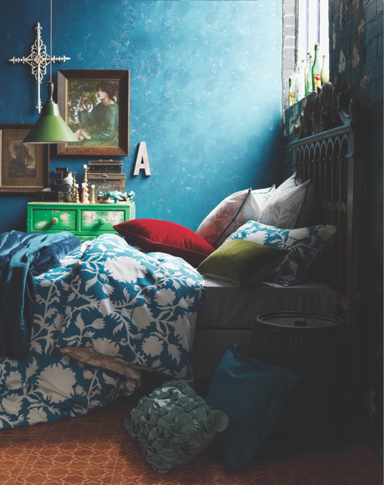 a colorful bedroom with a blue wall, a bed with colorful and printed bedding, a vintage green dresser, some artwork and accessories