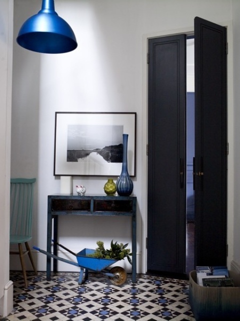 a catchy entryway with a bold Moroccan tile floor, a black console table, blue touches and midnight blue doors is a chic and lovely space