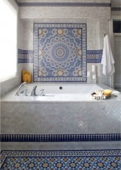 a refined neutral and bold blue bathroom with a bathtub clad with tiles, a Moroccan tile floor and decor clad on the wall plus some neutral textiles