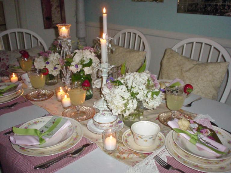 A vintage neutral and pastel colored tablescape with with a floral runner, pink placemats, floral porcelain, neutral blooms and candles, pastel napkins