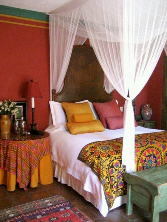 a bright Eastern bedroom in red, pink, ocher, with a dark stained wooden bed and bright textiles