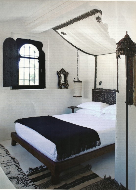 a black and white Moroccan bedroom with a shuttered window, a dark stained bed, a canopy and hanging lanterns