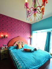 a colorful bedroom with a carved wooden bed, bright bedding, wall and chandelier and an ornate nightstand