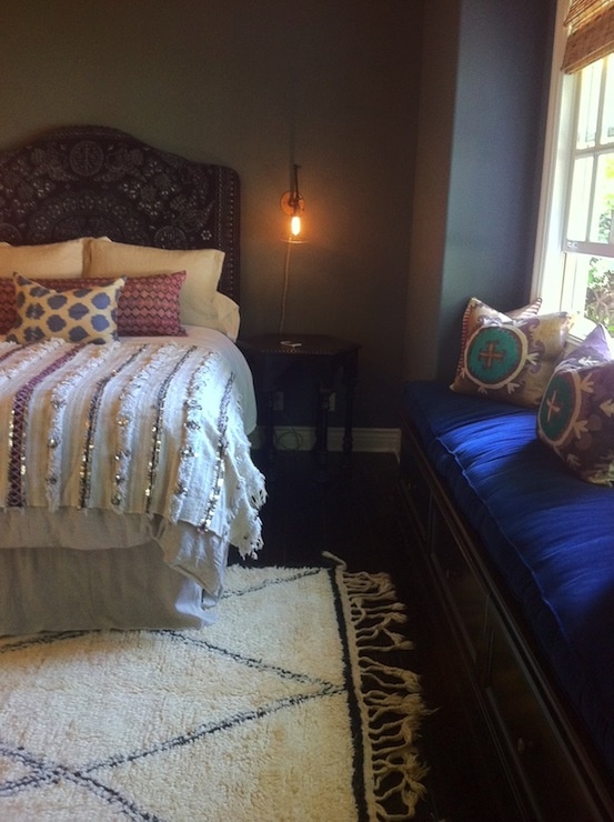 a moody Moroccan bedroom with an ornate headboard bed, a velvet upholstered seat and colorful cushions and bedding