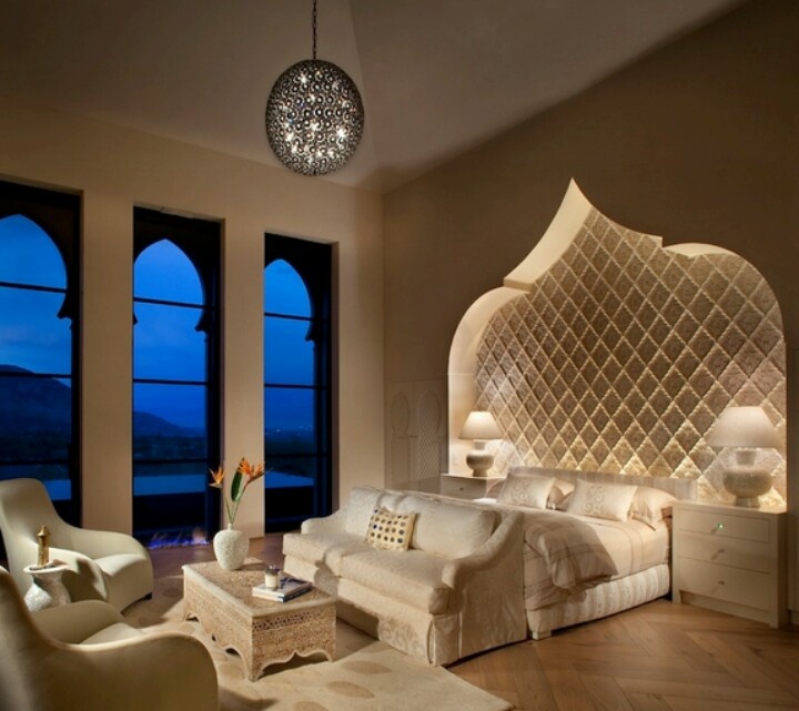 A luxurious Moroccan bedroom with a carved out headboard wall, Moroccan inspired windows and a carved wooden table