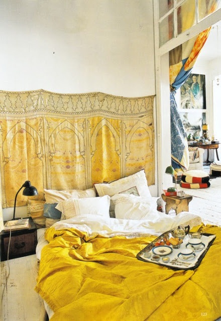 A small mustard sprinkled bedroom with a blanket on the wall and matching bedding plus vintage nightstands