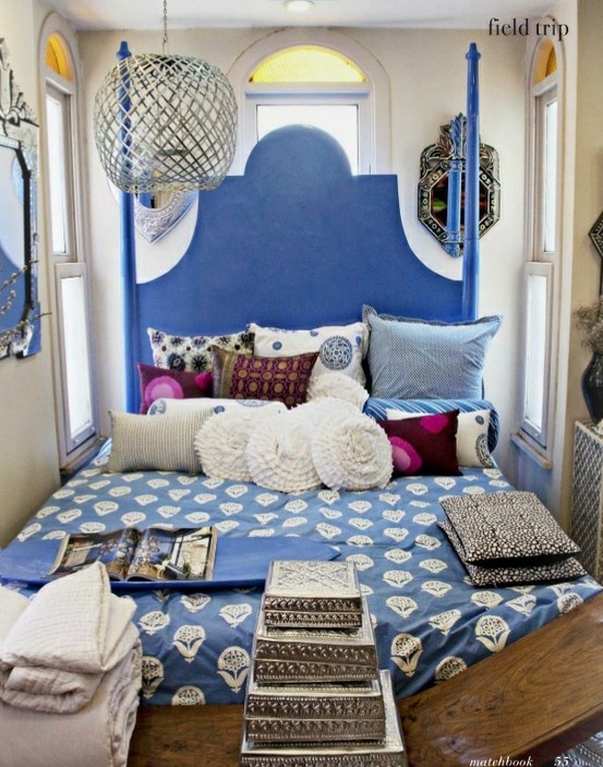 a small blue bedorom with an ornate bed, printed bedding and pillows, artworks and a lantern for an Eastern look