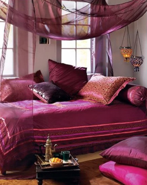 a bold purple and fuchsia bedroom with airy and sheer textiles, lanterns and a low table