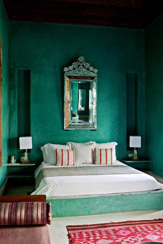 an emerald green Morocccan bedroom with plaster walls, printed textiles, an ornate mirror and elegant lamps