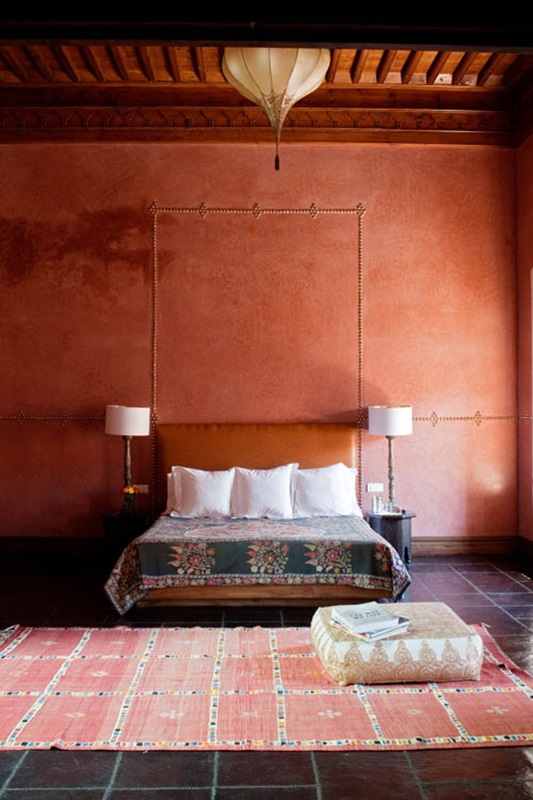 A rust colored and red Moroccan living room with a leather bed, a boho rug and a lantern