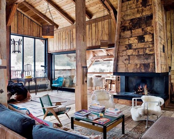 a modern chalet living room clad with wood, with a fireplace, some stylish furniture, boho and mid-century and layered rugs